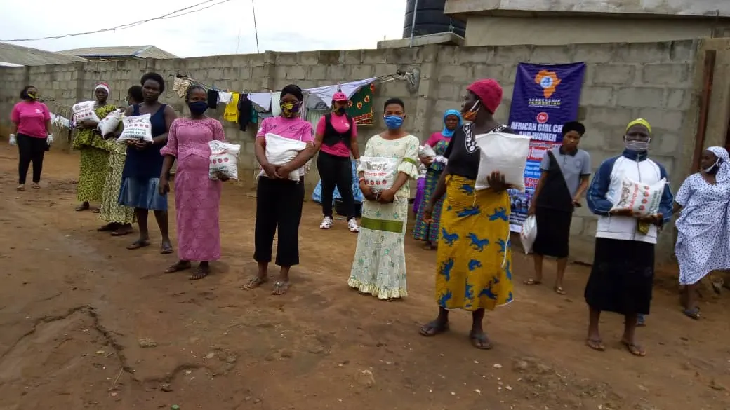 Community women wearing face masks stand in a socially-distanced line, each holding a bag of rice received from the foundation.
